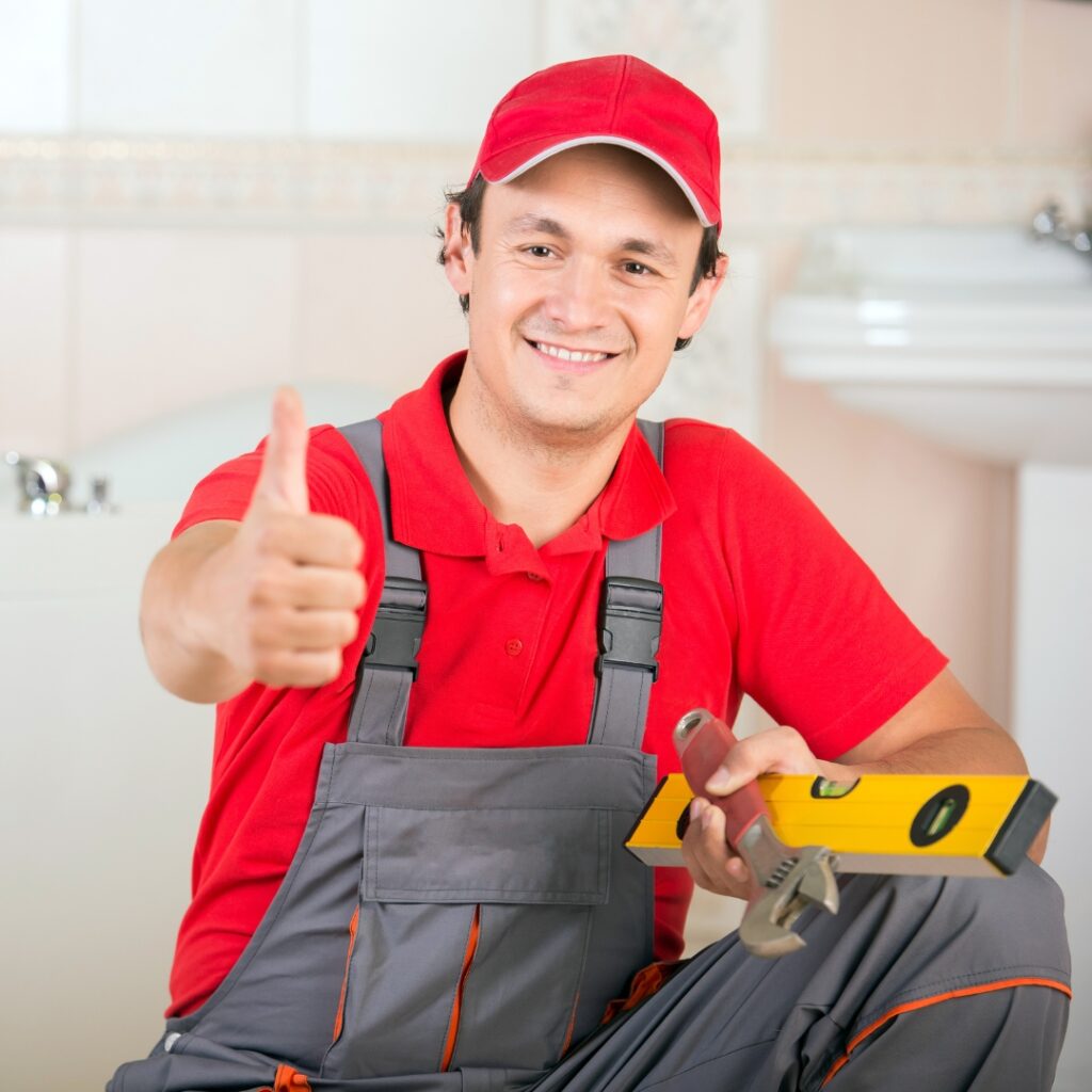 plumber smiling and holding a thumbs up while holding tools